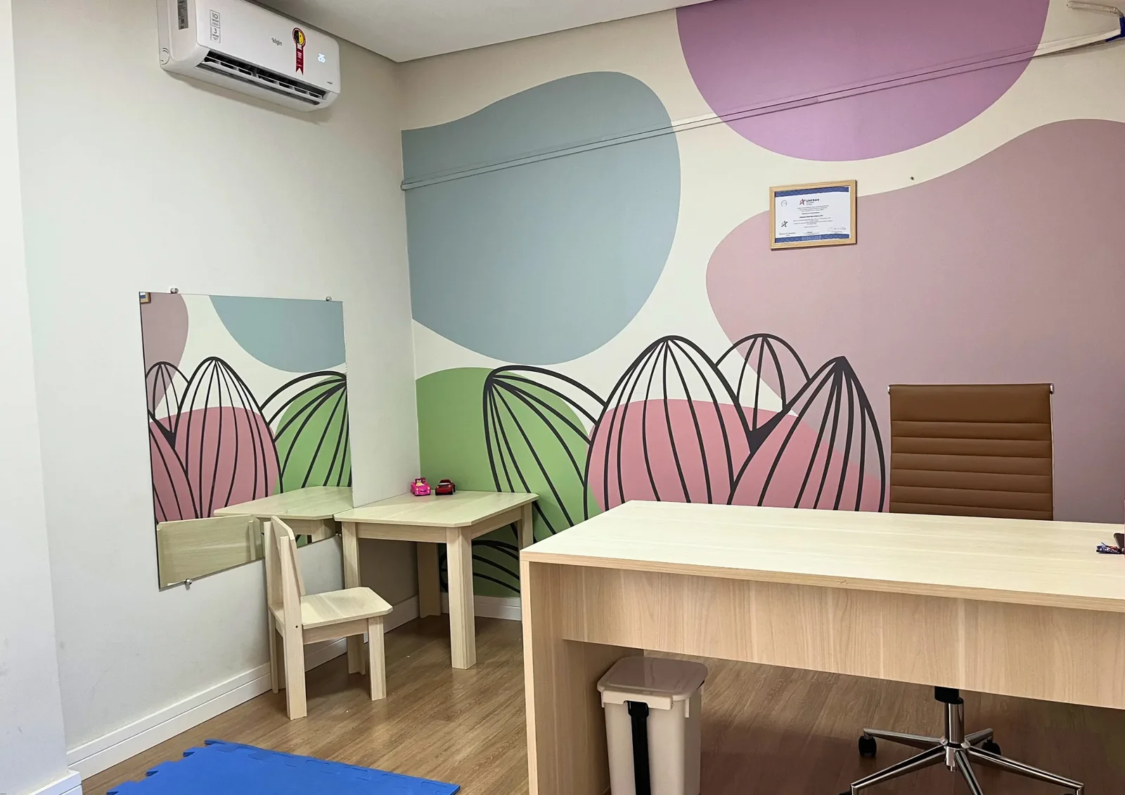 Sala de atendimento com parede colorida, mesa e cadeiras de madeira.