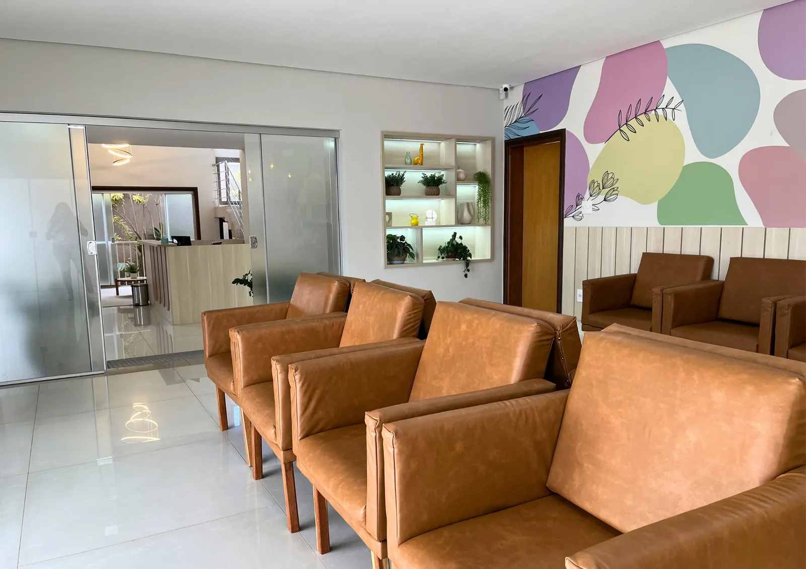 Sala de espera com poltronas de couro caramelo e divisória de vidro.