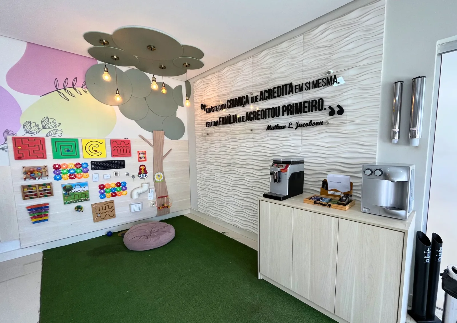 Sala de atividades com parede colorida, painel de comunicação alternativa e armários.