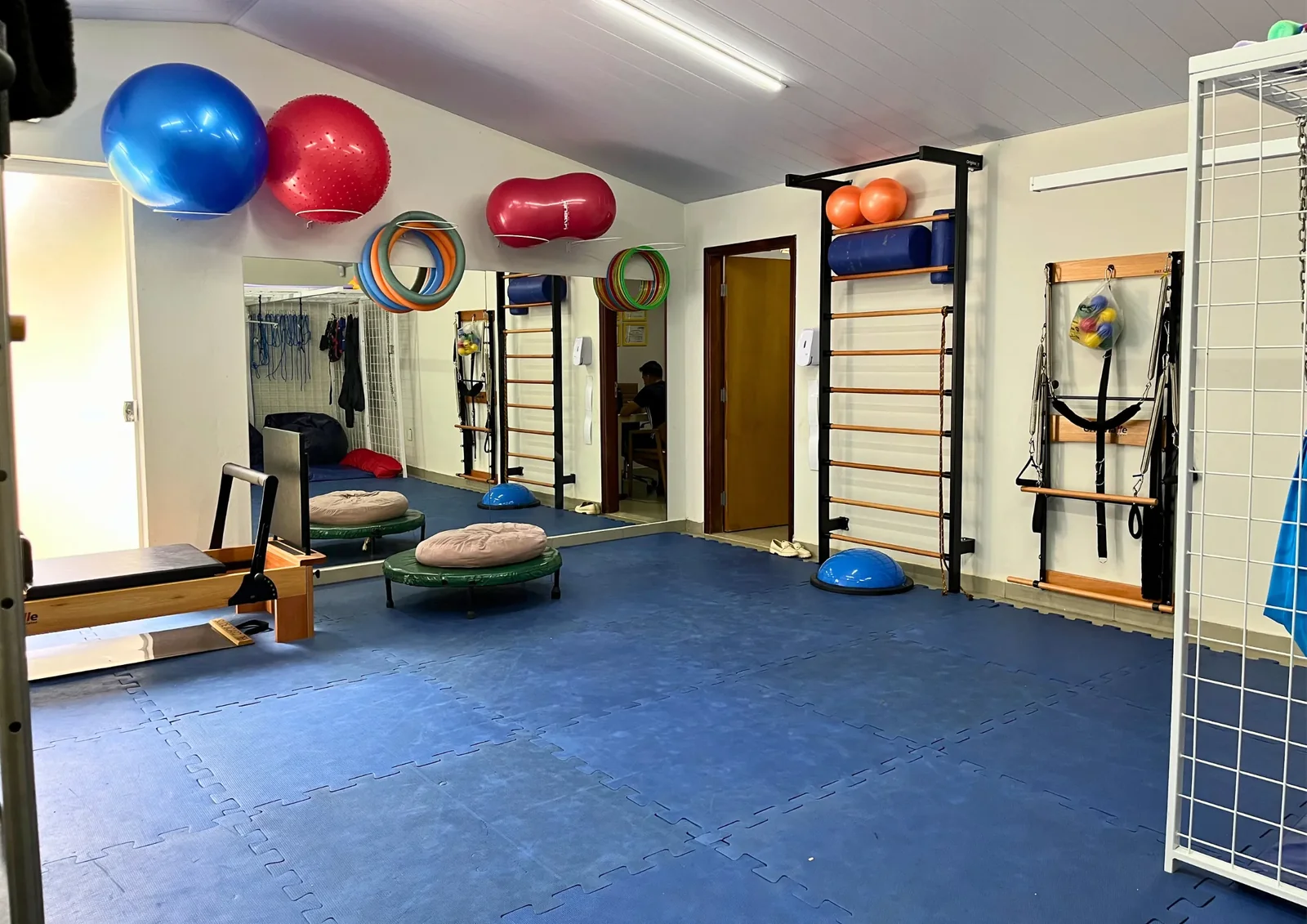 Sala de terapias com bolas suíças, espaldar e equipamentos de reabilitação.